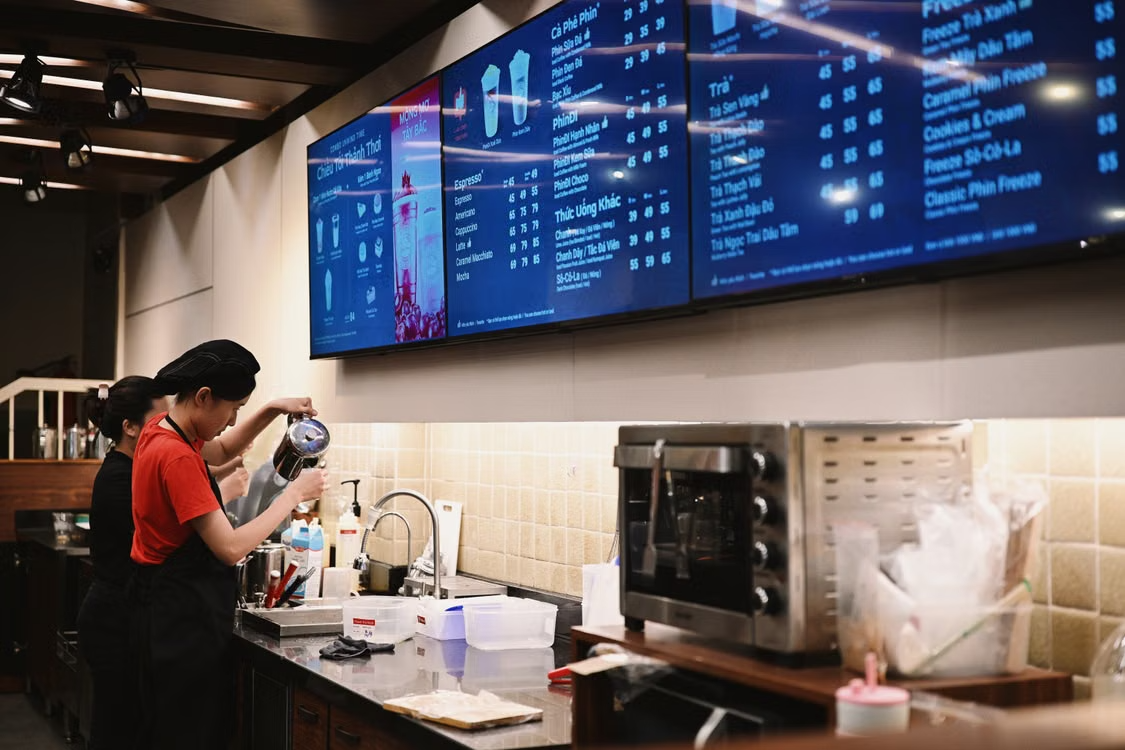 Nhân viên pha chế trong quán cà phê với bảng menu điện tử